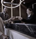 Rececionista de hotel a entregar cartão de quarto a hóspedes sorridentes, simbolizando o sucesso operacional.