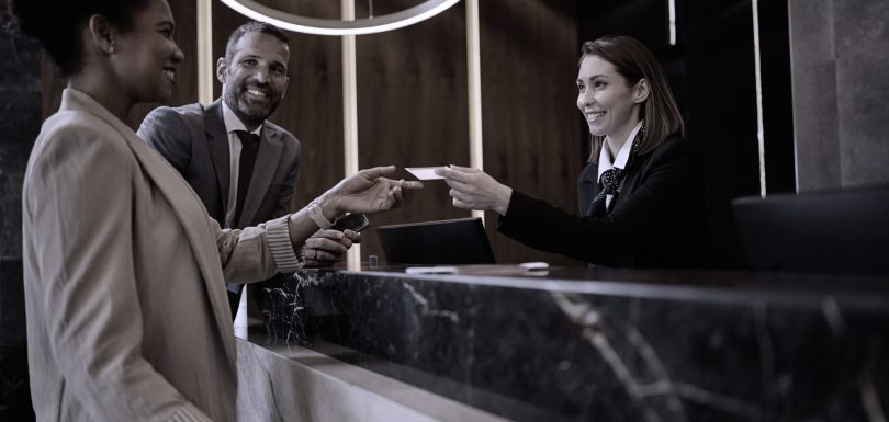 Rececionista de hotel a entregar cartão de quarto a hóspedes sorridentes, simbolizando o sucesso operacional.